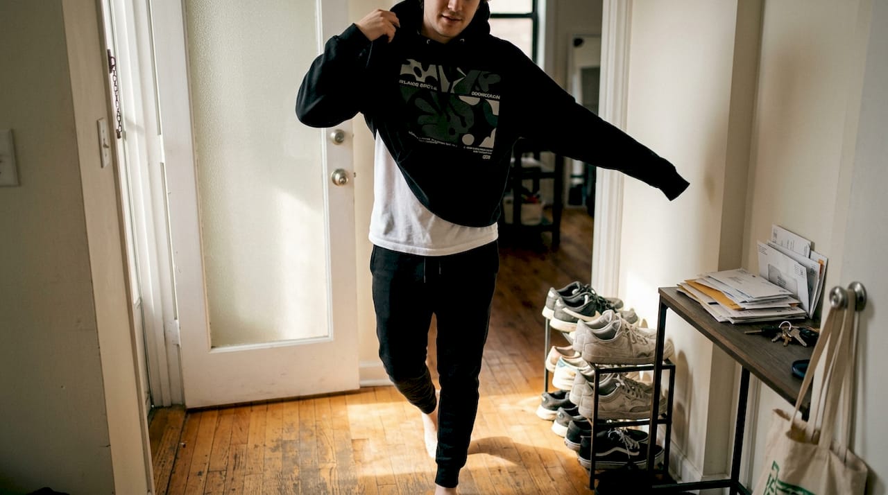Person layering streetwear hoodie with basics in apartment